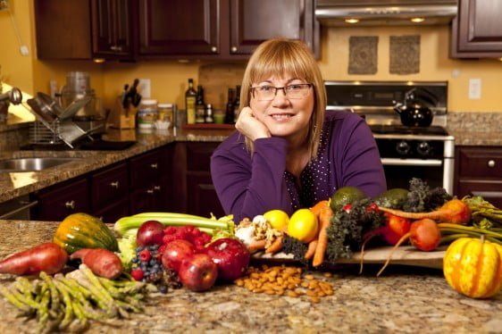 Anne Baker leaning on a kitchen counter that is full of fresh produce