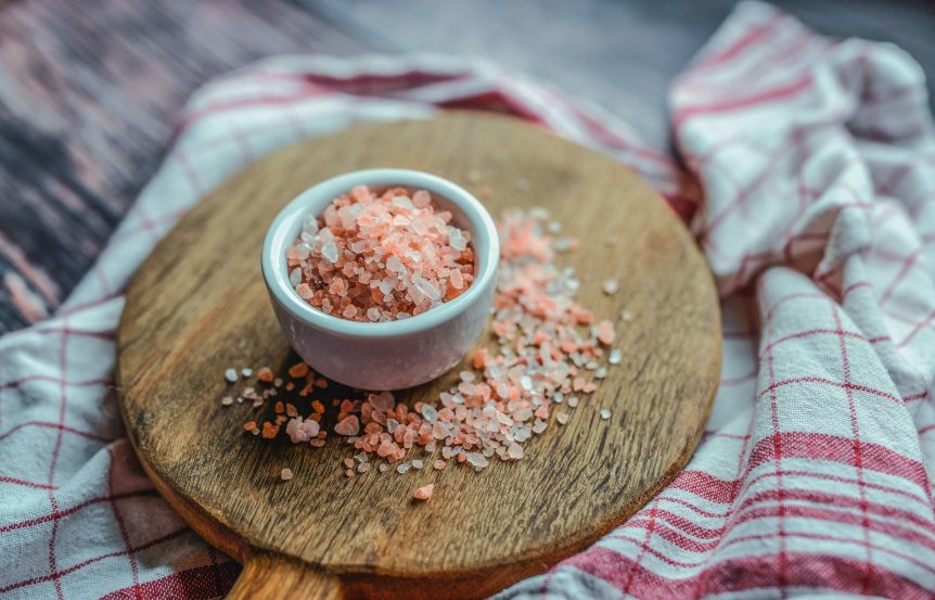 A white ramekin of pink salt on a wooden board on red and white dish towels
