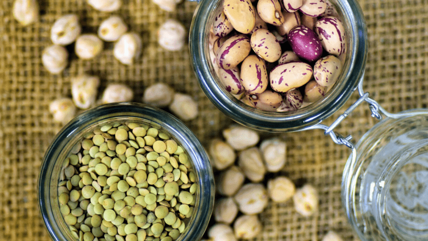 Green lentils and beans in two jars on a burlap tablecloth