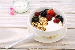 A white bowl of yogurt with raspberries, blackberries, and granola on a wooden table