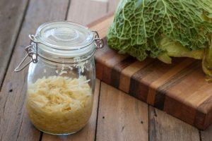 A jar of fermented kraut in a jar next to a cutting board with cabbage on it