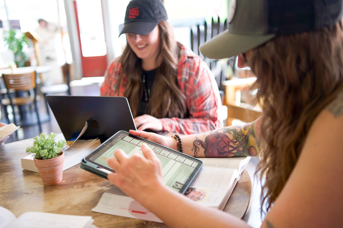 Online nutrition school students from Nutrition Therapy Institute studying at a coffee shop with an iPad and laptop.