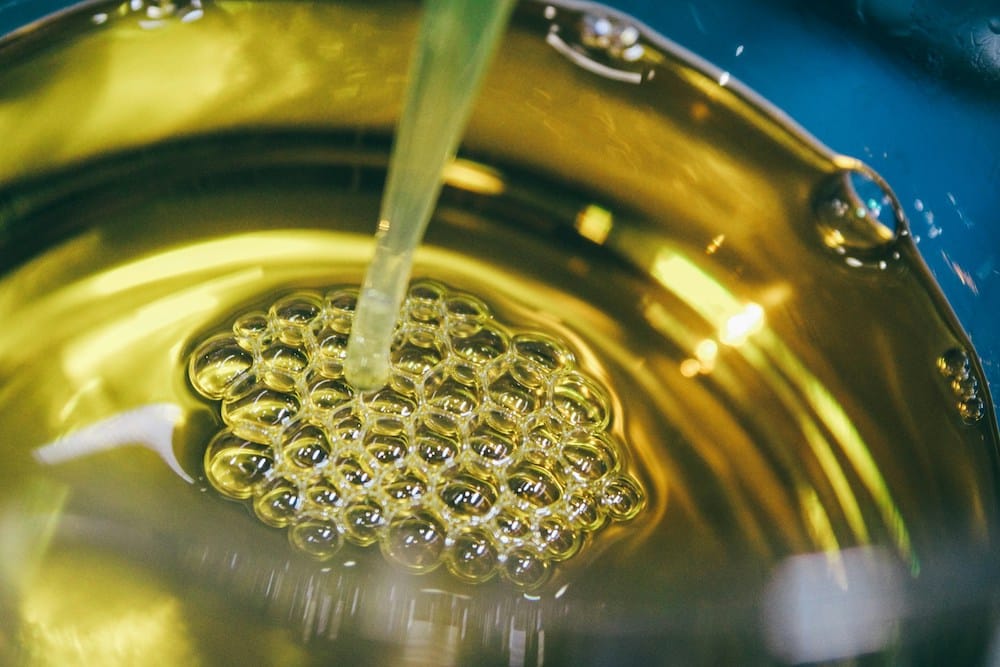 Glass of oil with a straw and bubbles, symbolizing processed oils and the discussion of trans fats and healthy alternatives in food.
