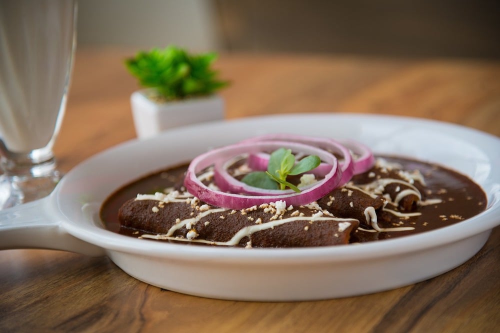 Mexican enchiladas topped with sliced onions, a dish often served with mole sauce made from nuts and seeds.
