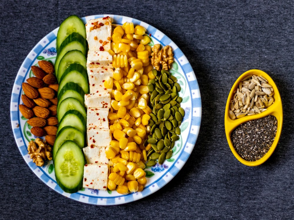 Healthy snack of sliced cucumber with nuts and seeds on a white and blue ceramic plate.
