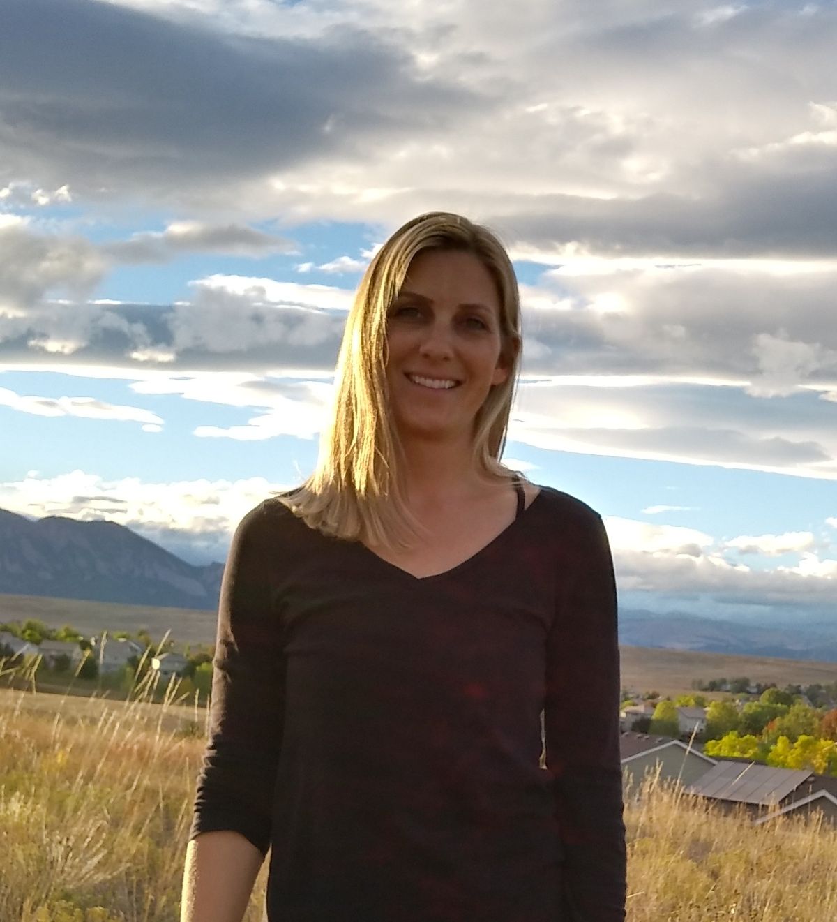Cassie Kerr has short blonde hair and is standing outside in front of the sky and mountains