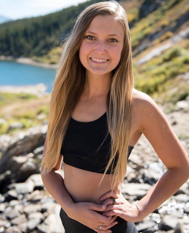 Rosie Christian has long blonde hair and is standing in front of a lake outside